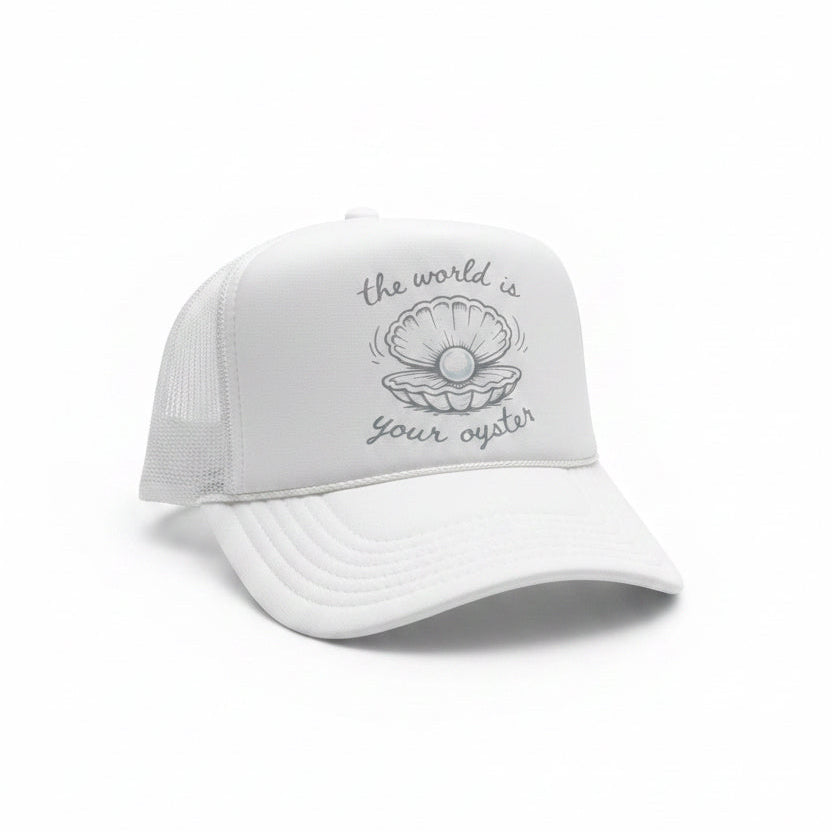 A white trucker hat with a printed design on the front panel. The design features a blue gray clamshell illustration with the text 'the world is your oyster' written in a cursive font.