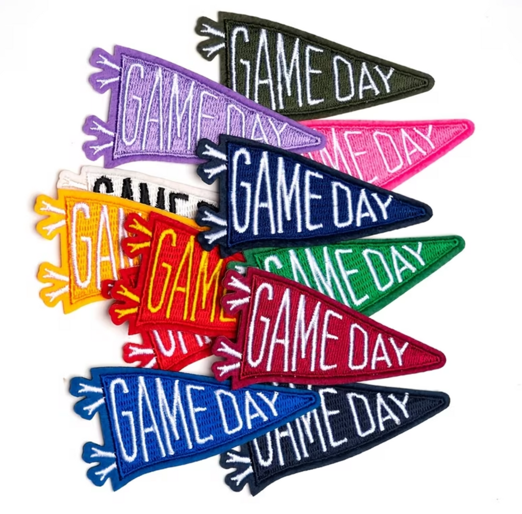 Six colorful embroidered 'GAME DAY' pennant patches in different colors (green, pink, purple, red, orange, blue) arranged on a white background.