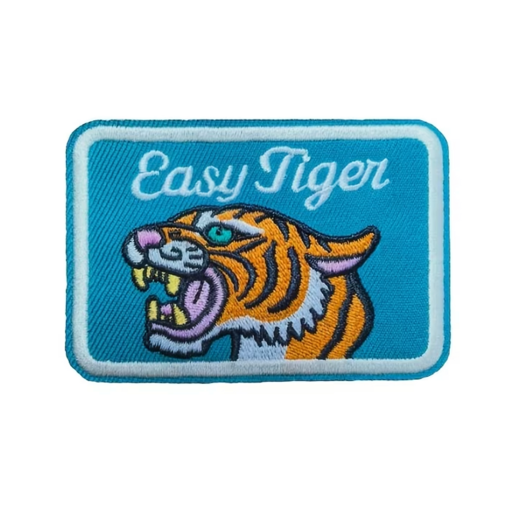 An embroidered rectangular patch featuring a tiger head and the words 'Easy Tiger' on a light blue background, shown centered on a white screen area within a phone chat screenshot.