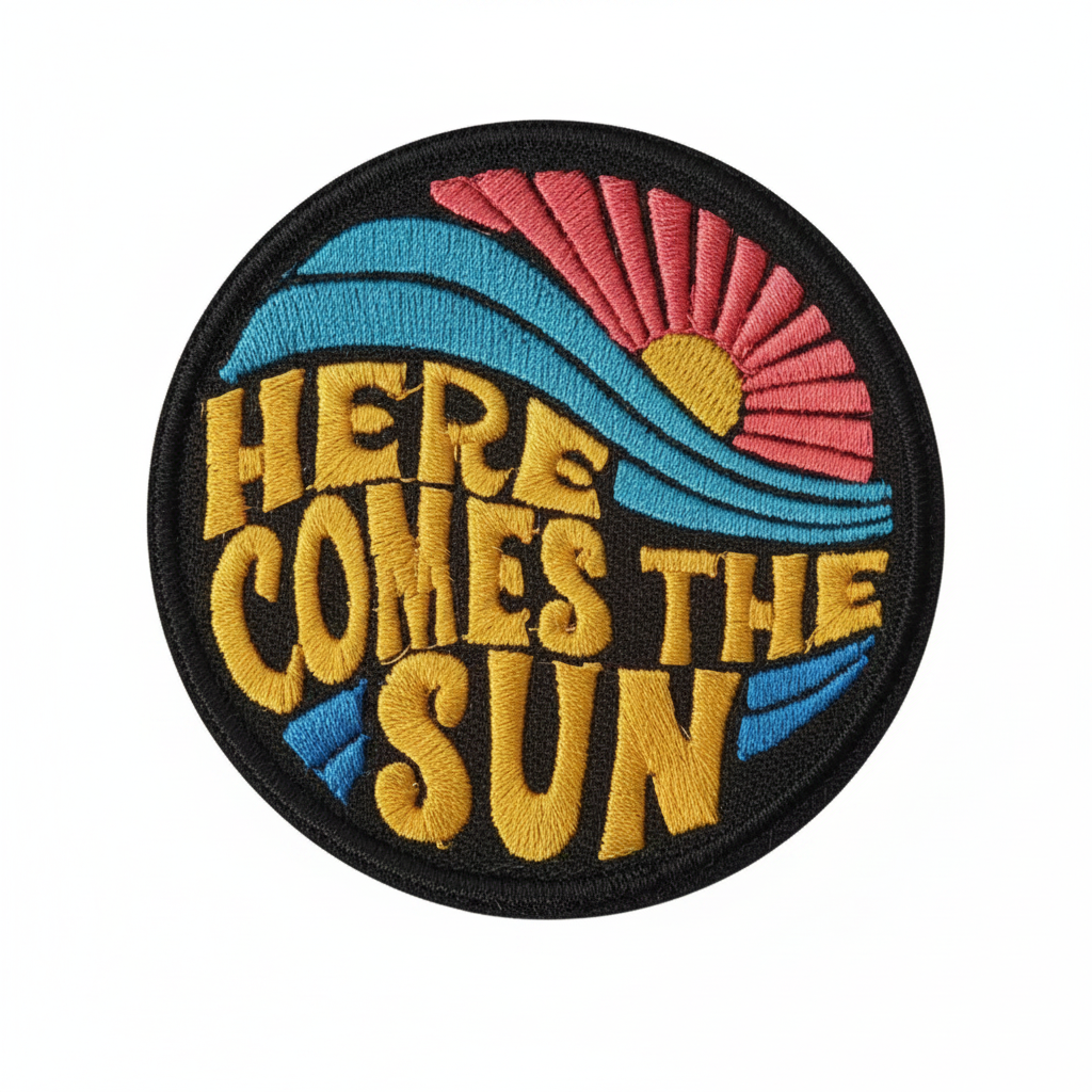 A product listing image showing a circular embroidered patch with the text 'HERE COMES THE SUN' in yellow, with blue and pink wave details, on a white background with the text '6pcs' above it.
