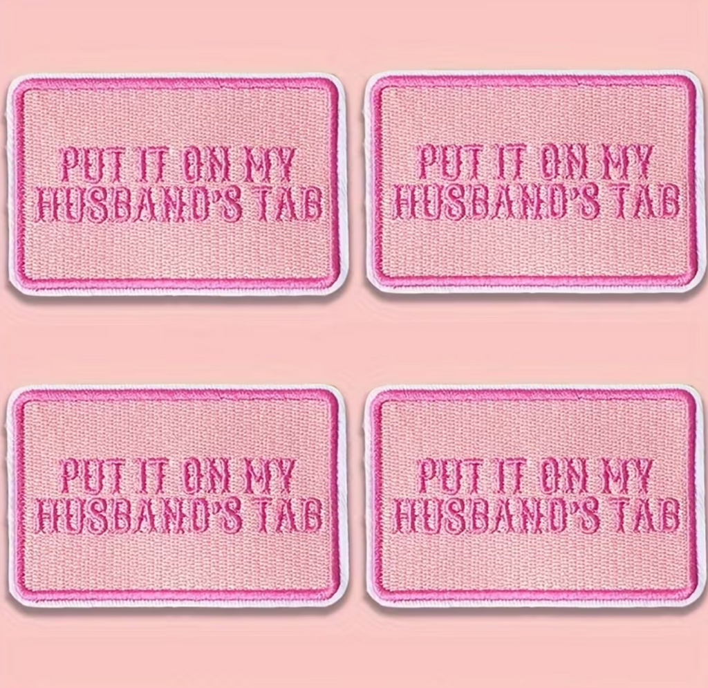 Four pink rectangular patches with rounded corners, each reading 'PUT IT ON MY HUSBAND'S TAB' in pink lettering, arranged in a 2x2 grid on a pink background.