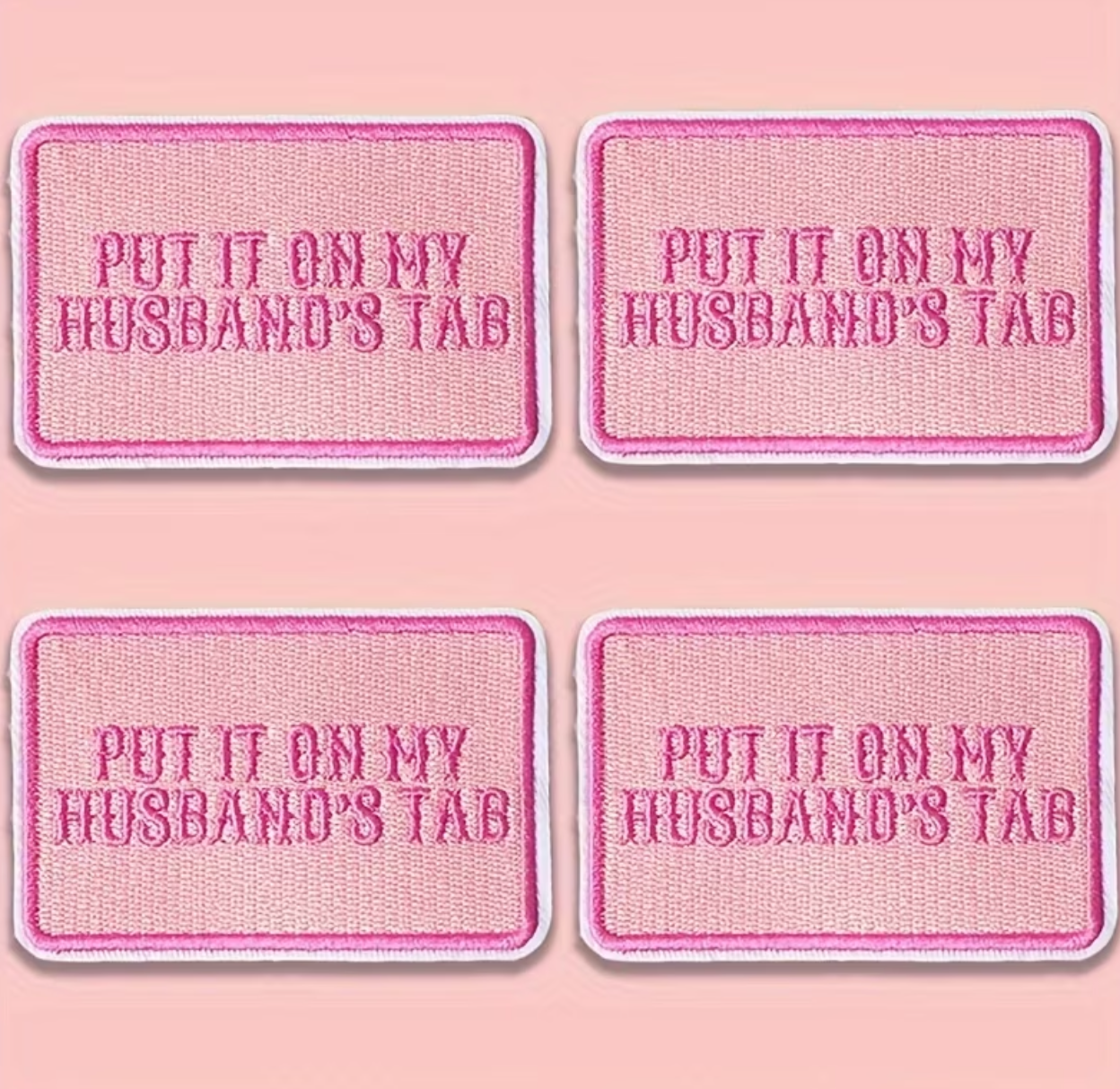 Four pink rectangular patches with rounded corners, each reading 'PUT IT ON MY HUSBAND'S TAB' in pink lettering, arranged in a 2x2 grid on a pink background.