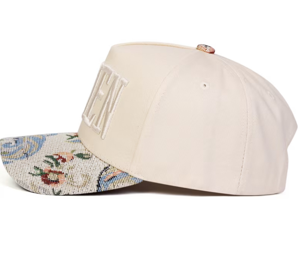 A cream-colored baseball cap with a floral-patterned brim and large embroidered lettering on the side, shown against a plain white background.